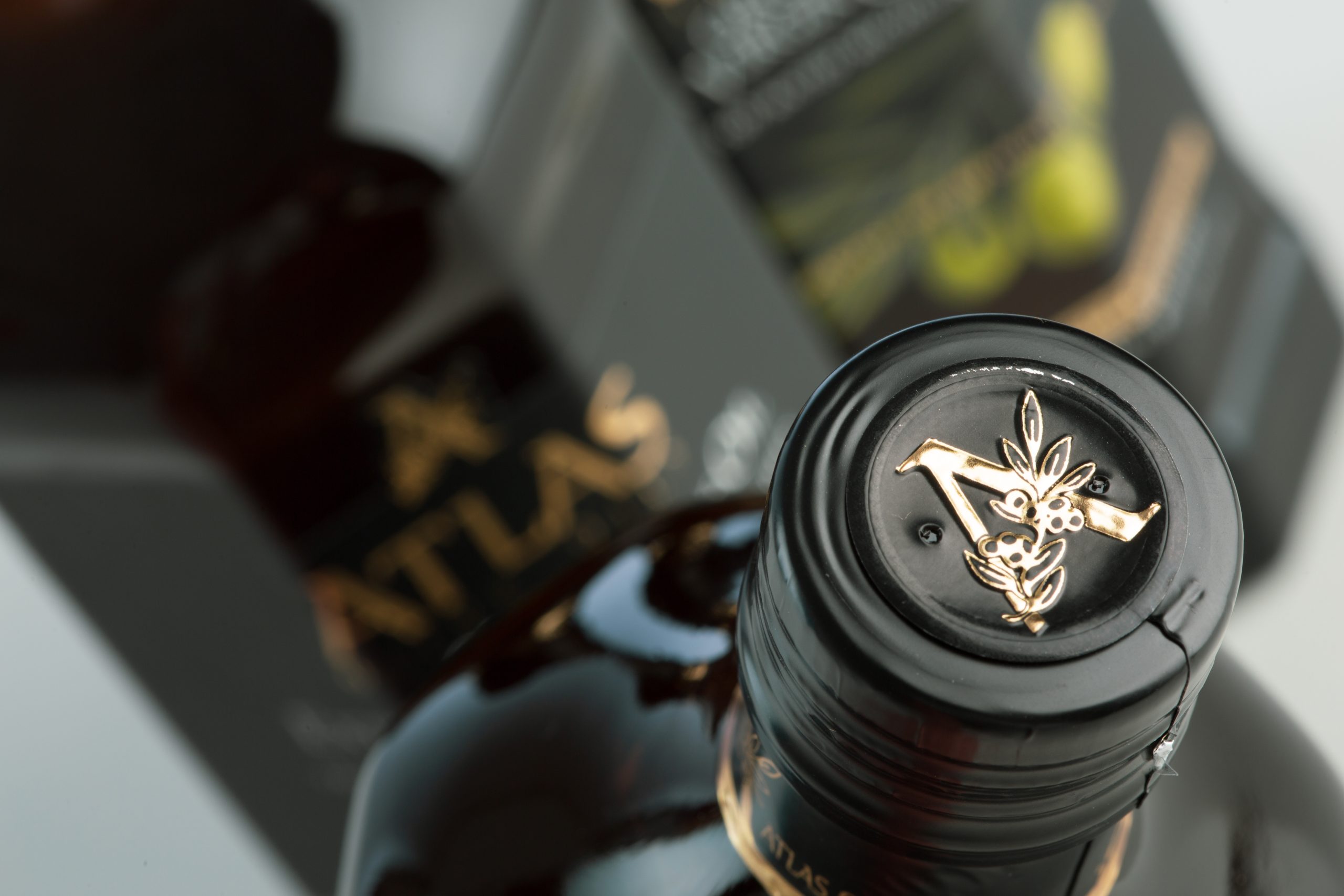 Close-up of a dark bottle neck with black foil and a gold decorative emblem, blurred background.